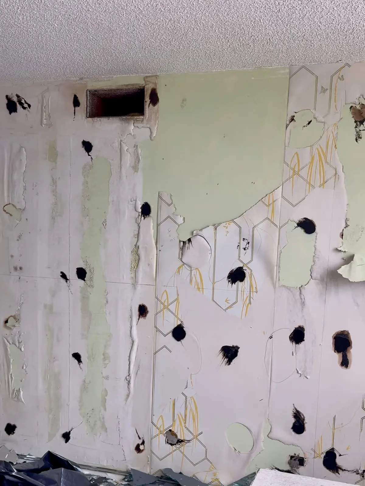 Wall with peeling wallpaper and damaged drywall before repair